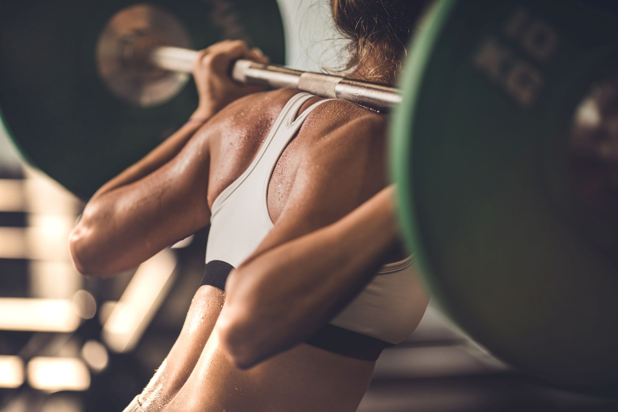 A person in athletic wear is performing a squat with a barbell loaded with weights on their shoulders.