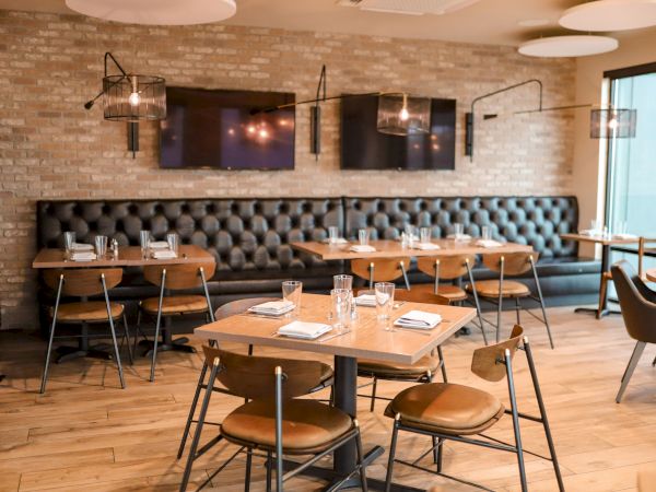 The image shows a modern restaurant interior with wooden tables, cushioned seating, elegant lighting, and a cozy ambiance.