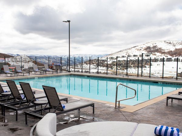 Outdoor swimming pool with lounge chairs, snowy mountains in the background, and a cloudy sky above, creating a tranquil scene.