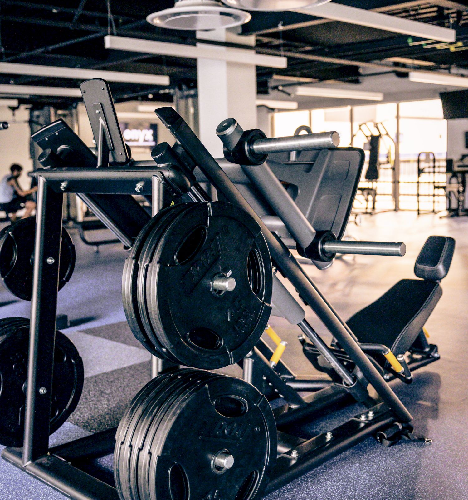 A modern gym weight rack with multiple stacked plates and a leg extension machine in a spacious, well-lit workout area.
