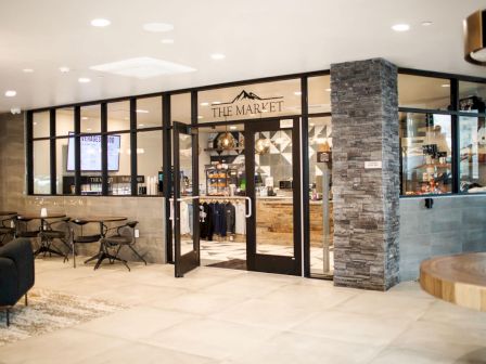 The image depicts a modern, inviting market entrance in a commercial space with glass doors and various items inside.