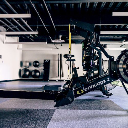 A modern gym with a person using a stationary bike, bright lighting, and fitness equipment visible in the background.