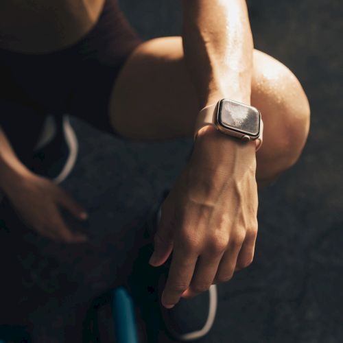 A person wearing a smartwatch sits on exercise equipment, possibly resting after a workout.