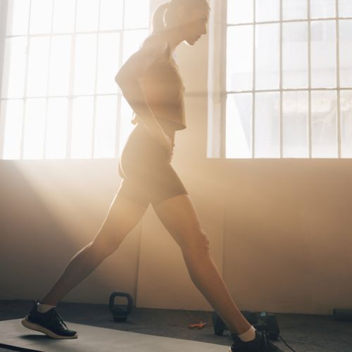 A person is stretching on a yoga mat in a sunlit room, with kettlebells in the background.