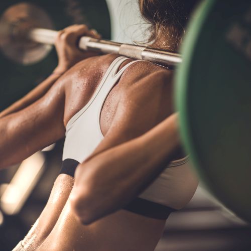 A person in workout gear is performing a squat with a barbell loaded with weights, focusing on strength training.