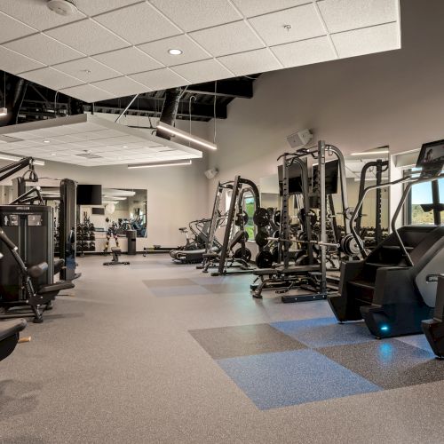 A modern gym with weight machines, cable equipment, treadmills, and bright ceiling lights.