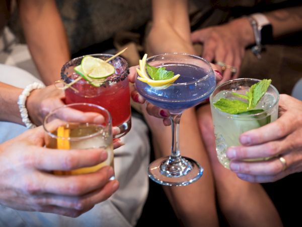 A group of people holding colorful cocktails with lime garnishes, clinking glasses together at a social gathering.