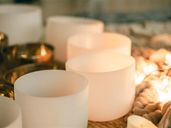 Soft candlelight glows among white frosted bowls and warm stones, creating a peaceful, cozy spa-like ambiance.