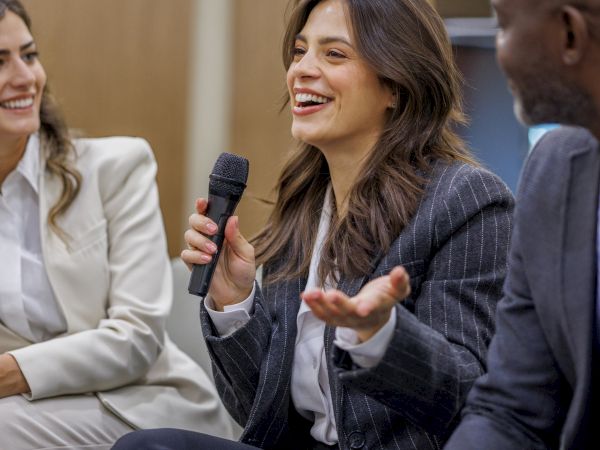A woman speaks into a microphone during a panel discussion, with others listening and smiling.