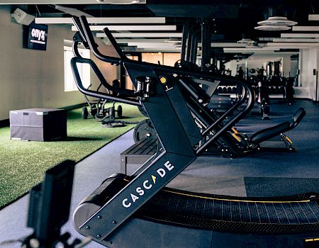A row of high-end treadmills in a modern gym, blue flooring, dim ceiling lights, and equipment lining the room, ready for workouts.