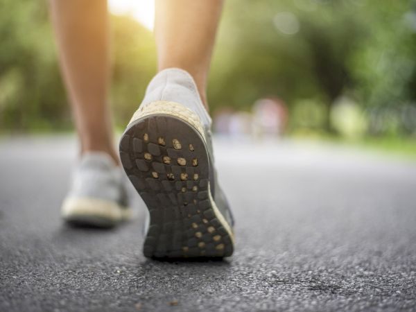 A person in sneakers walking away on a paved path, focus on the shoe tread, sunny park setting, calm stride.