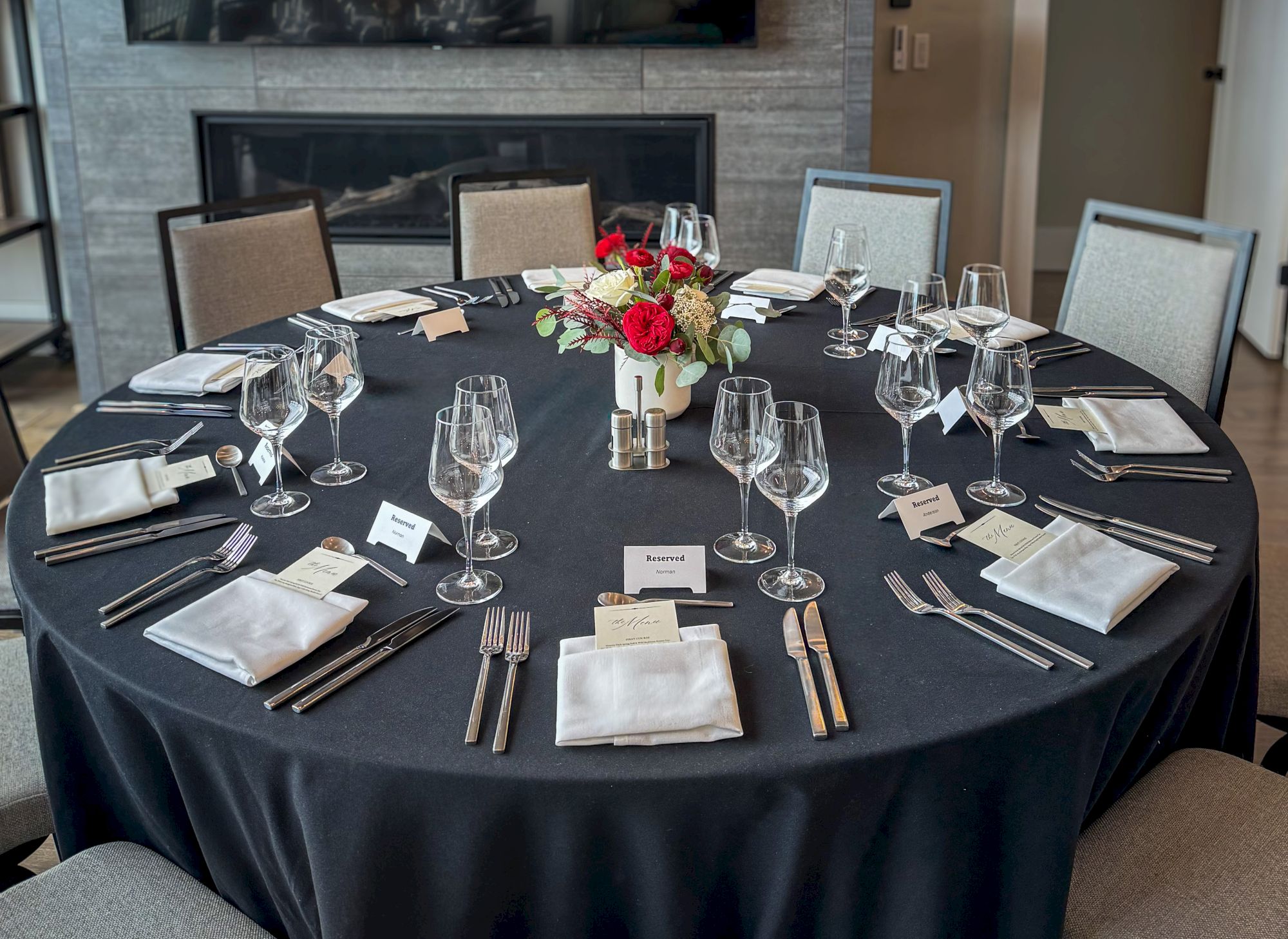 A formal dining table set with glassware, cutlery, place cards marked &ldquo;Reserved,&rdquo; and a centerpiece of red flowers.