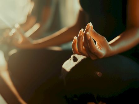 Two people&rsquo;s hands are clasped in a prayer-like gesture, lit by warm sunset glow, with a softly blurred background.