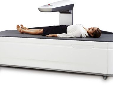 A man lies on a white mattress inside a box-style bed, with a headrest and adjustable base.